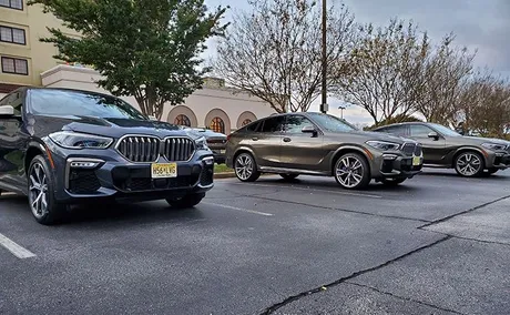 Three parked BMW SUVs in a parking lot, set against a backdrop of trees and a building.