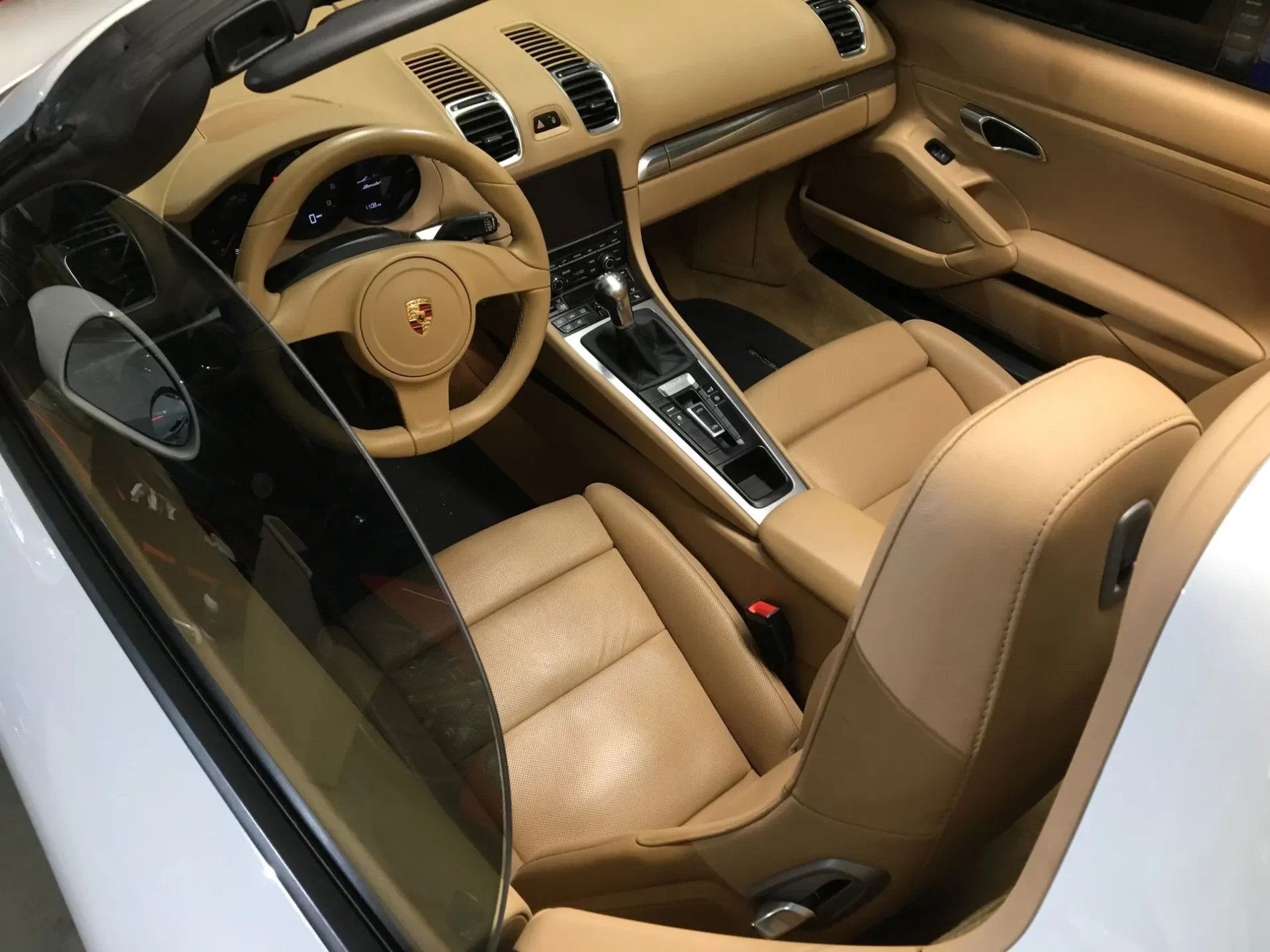 Interior of a luxury sports car featuring beige leather seats, a multifunction steering wheel, and a sleek central console with a Porsche emblem on the steering wheel.